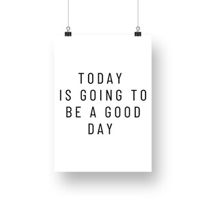 K&ouml;nnte beinhalten: Ein wei&szlig;es Poster mit dem Text "TODAY IS GOING TO BE A GOOD DAY" in Schwarz, das an zwei schwarzen B&uuml;roklammern h&auml;ngt. Das Poster ist vor einem wei&szlig;en Hintergrund zentriert.