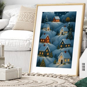 May include: A framed print of a winter village scene. The artwork depicts snow-covered hills with illuminated houses, evergreen trees, and a starry night sky. The houses have red, blue, and white exteriors.
