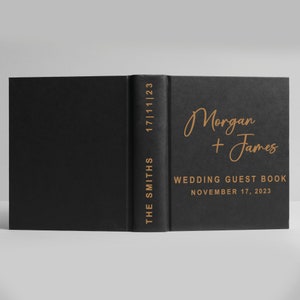 May include: Black wedding guest book with gold lettering. The names Morgan and James are written in cursive with the text "Wedding Guest Book" and "November 17, 2023" below.