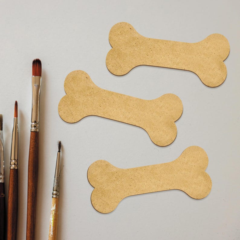 May include: Three brown cardboard dog bone shapes on a white surface. Five paintbrushes are arranged vertically on the left side of the image.