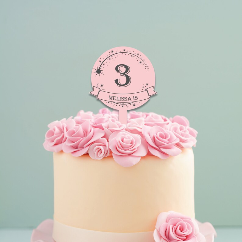 May include: Pink cake with pink frosting and a pink and gray cake topper that says "Melissa is 3" with a star and a shooting star design.