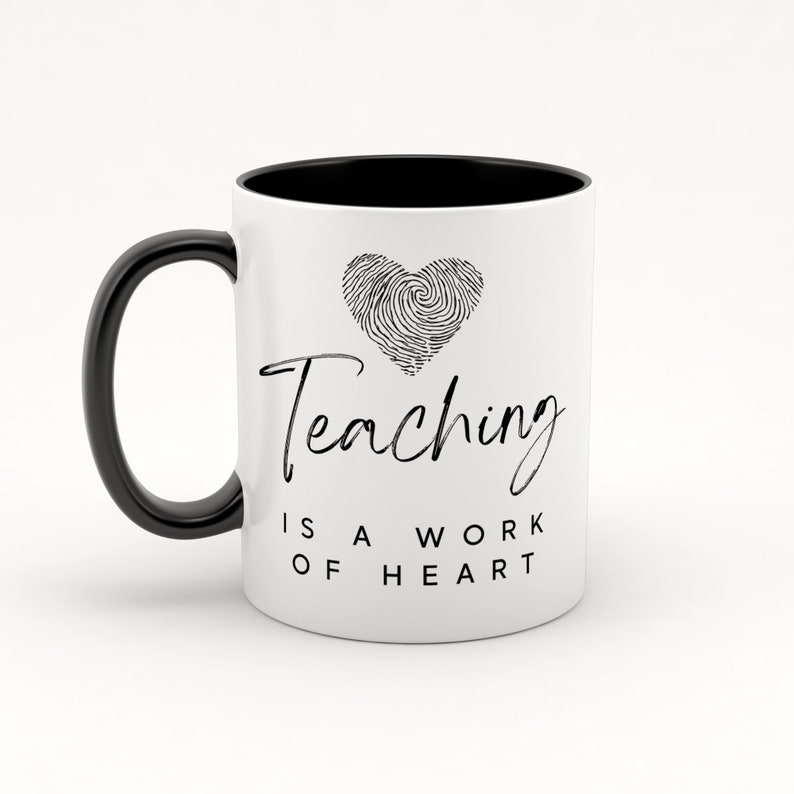 Puede incluir: Taza de cer&aacute;mica blanca con asa e interior negros. La taza presenta el texto "Teaching is a work of heart" en escritura negra, junto con un dise&ntilde;o de coraz&oacute;n de huellas dactilares. Un regalo atento para profesores.