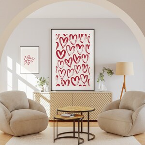 May include: A living room interior with two armchairs, a coffee table, and a framed print of red hearts on a white background. The print is hanging on a wall above a wooden cabinet. The text "I love you" is written on a smaller framed print on the wall.