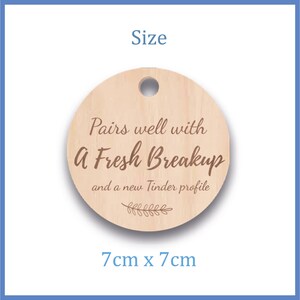 May include: A round wooden tag with a hole at the top. The tag has the text "Pairs well with A Fresh Breakup and a new Tinder profile." The tag measures 7cm x 7cm.