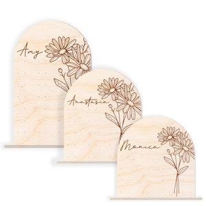 May include: Three wooden arch-shaped signs with a floral design and names "Amy", "Anastasia", and "Monica" written in cursive.