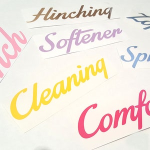 May include: Assortment of colorful vinyl lettering labels for home organization. The labels read "Hinch", "Cleaning", "Softener", "Spray", "Comfort", "Hinch", and "Loft" in a variety of colors.