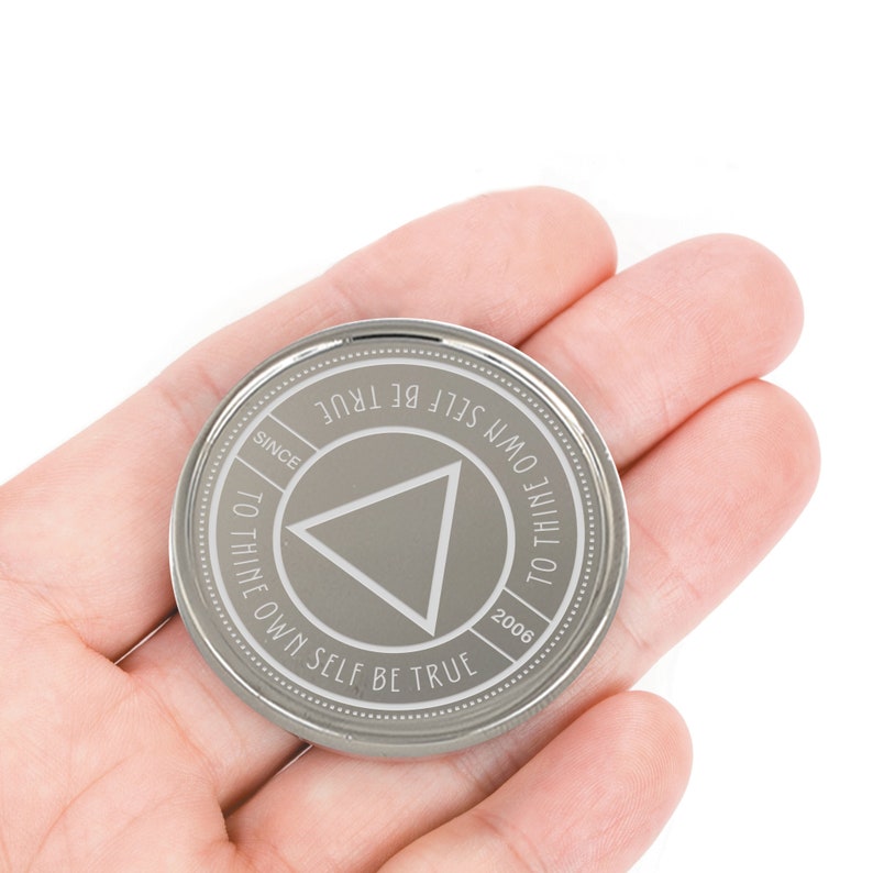 May include: A silver coin with the inscription "To thine own self be true" and a triangle in the center. The coin also has the inscription "Since 2006".