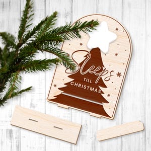 Puede incluir: Calendario de adviento de madera con un &aacute;rbol marr&oacute;n y el texto "Sleeps till Christmas". El calendario tiene una estrella blanca en la parte superior y una ranura para cada d&iacute;a hasta Navidad.