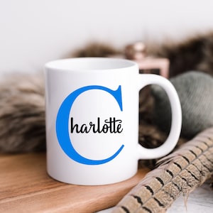 K&ouml;nnte beinhalten: Wei&szlig;e Keramiktasse mit einem blauen 'C' und dem Namen 'charlotte' in schwarzen Buchstaben.