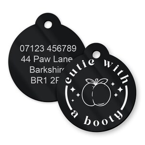 May include: Black pet tag featuring the phrase "cutie with a booty" and a peach graphic. The tag also displays a phone number and address in white text.