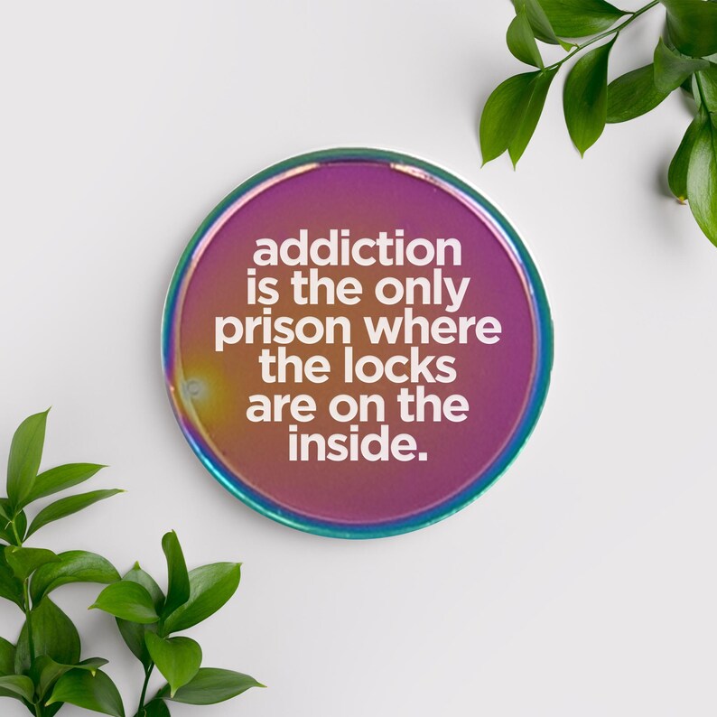 May include: A round, iridescent pink and purple coaster with the quote "addiction is the only prison where the locks are on the inside."