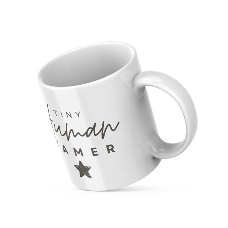 May include: White ceramic mug with a black design that says "Tiny Human Gamer" with a small star below the text.