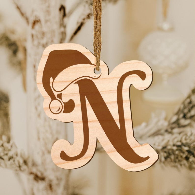 May include: Wooden Christmas ornament shaped like the letter "N" with a Santa hat design. The ornament is made of light-colored wood with a brown letter and hat. A brown string is attached for hanging.