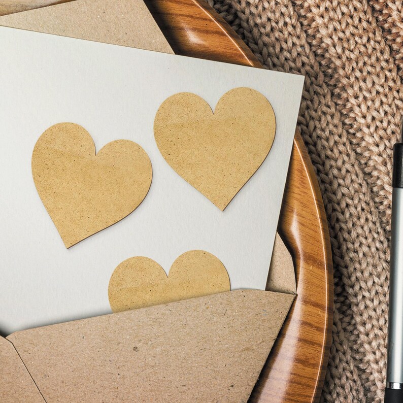 Op de afbeelding: Een witte kaart met drie bruine papieren hart stickers erop. De kaart ligt op een houten bord en een bruin gebreid oppervlak.