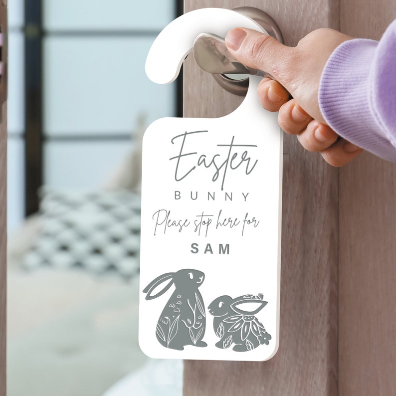 May include: White door hanger with a gray bunny rabbit design. The hanger says "Easter Bunny Please stop here for SAM".