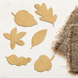 May include: A set of seven brown cardboard cutouts of autumn leaves and an acorn. The cutouts are arranged on a white background with a piece of hessian fabric in the top right corner.