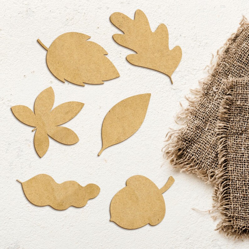 May include: A set of seven brown cardboard cutouts of autumn leaves and an acorn. The cutouts are arranged on a white background with a piece of hessian fabric in the top right corner.