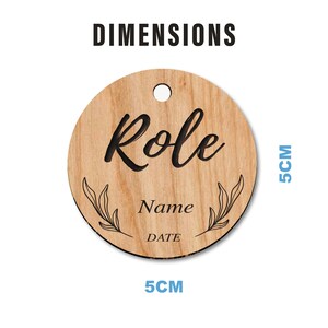 Puede incluir: Una etiqueta redonda de madera con un agujero en la parte superior. La etiqueta tiene un di&aacute;metro de 5 cm y presenta la palabra "Rol" en una fuente decorativa, seguida de las palabras "Nombre" y "Fecha". La etiqueta est&aacute; decorada con dos peque&ntilde;as ramas frondosas.