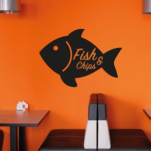Puede incluir: Silueta en blanco y negro de un pez con el texto "Fish & Chips" en una pared naranja. La imagen est&aacute; en un ambiente de restaurante con un banco y una mesa.