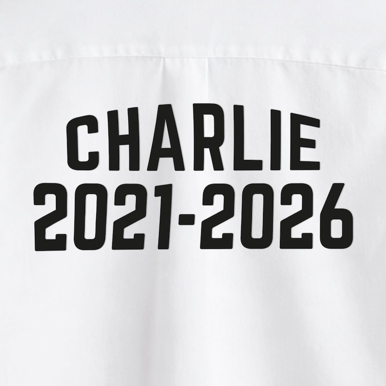 Puede incluir: Camiseta blanca con el nombre "CHARLIE" impreso en letras negras en negrita, junto con los a&ntilde;os "2021-2026". El texto est&aacute; centrado y es claramente visible en la prenda.