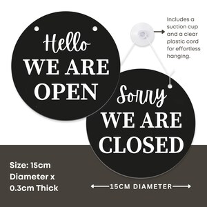 K&ouml;nnte beinhalten: Schwarzes rundes Schild mit wei&szlig;em Text "Hello WE ARE OPEN" und "Sorry WE ARE CLOSED". Das Schild hat einen Durchmesser von 15 cm und ist 0,3 cm dick. Inklusive Saugnapf und klarer Schnur zum Aufh&auml;ngen.