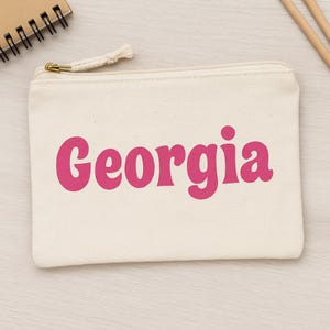 May include: A white canvas zippered pouch with a pink retro font that says "Georgia".