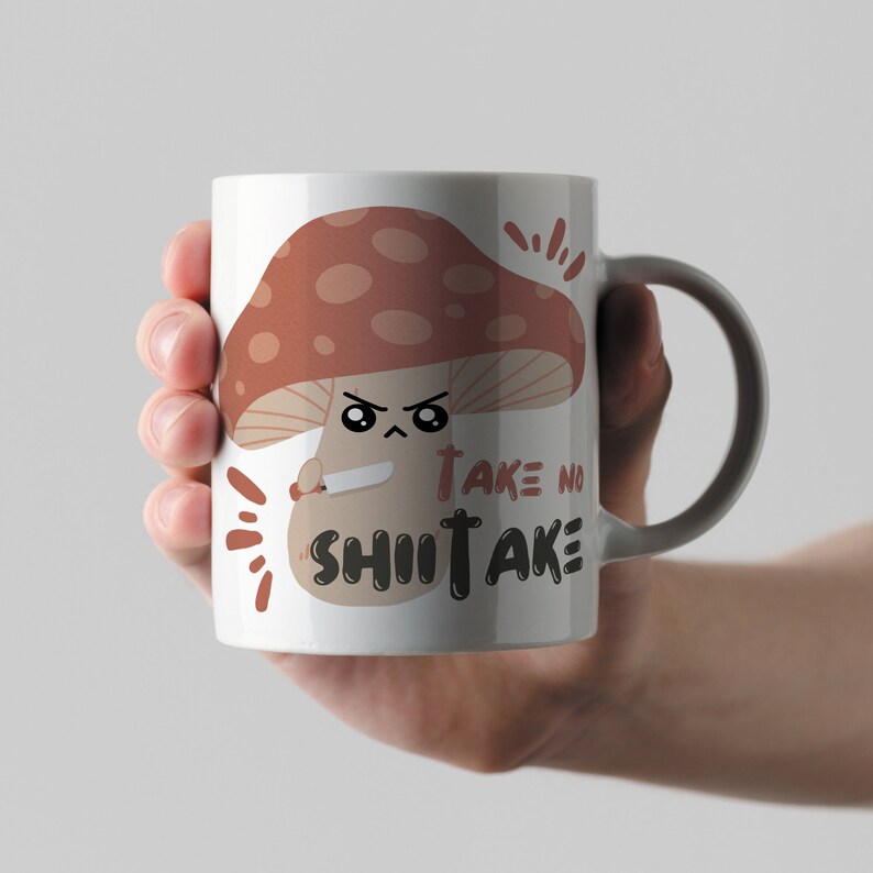 May include: White ceramic mug with a brown cartoon mushroom holding a knife. The mushroom has a face with angry eyes and the text "Take no Shitake" is printed below it.