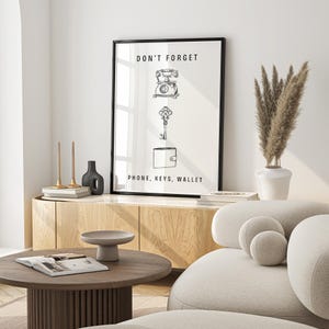 May include: Black and white illustration of a phone, keys, and wallet with the text "Don't forget phone, keys, wallet". The illustration is framed and hanging on a white wall.