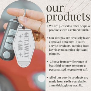 May include: A white acrylic keychain with the text "The Getaway Car" in black lettering. The keychain is in the shape of a motel key. The keychain is being held by a hand.