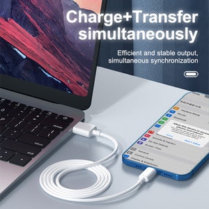 Op de afbeelding: Een witte oplaadkabel verbindt een laptop met een smartphone. Het smartphonescherm toont een bericht waarin wordt gevraagd of het apparaat toegang mag krijgen tot foto's en video's. De tekst "Charge + Transfer tegelijkertijd" wordt boven de afbeelding weergegeven.