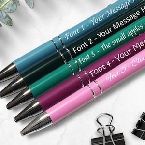 May include: Five pens with different colored barrels and silver accents. Each pen has a different font style and text, including "Font 1 - Your Message", "Font 2 - Your Message", "Font 3 - The small apples", "Font 4 - Your Message", and "Font 5 - Claim".