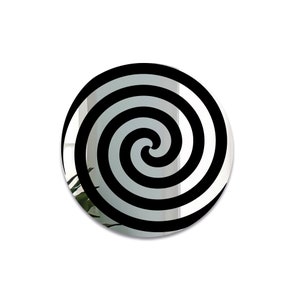 May include: A round mirror with a black and white spiral design. The mirror is reflective and shows a blurry image of a plant in the background.