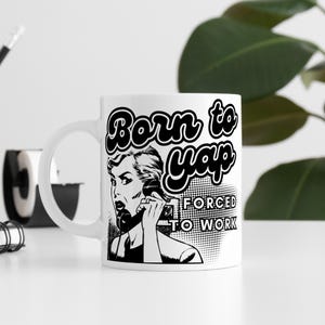 May include: White ceramic mug with a black and white illustration of a woman on the phone. The text "Born to yap Forced to work" is printed on the mug.
