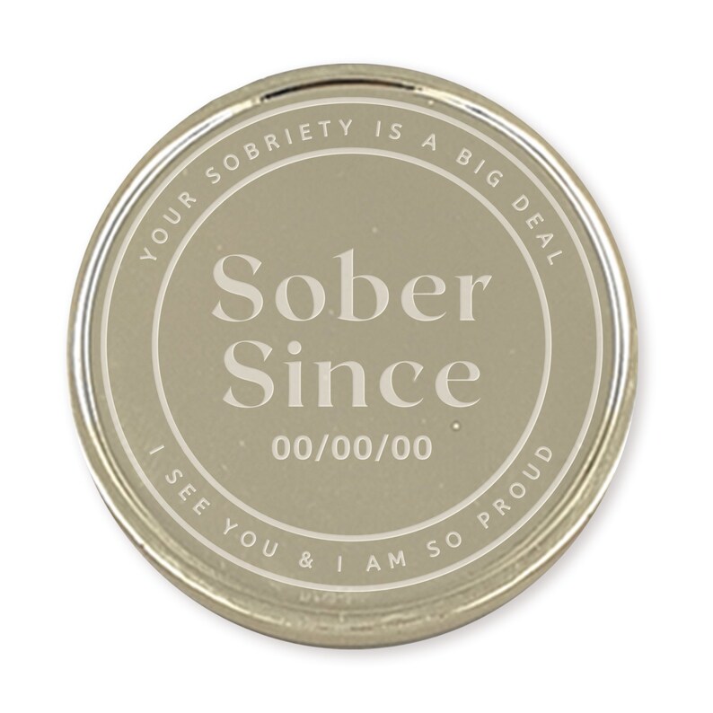 May include: A silver-colored round coin with the text "YOUR SOBRIETY IS A BIG DEAL" and "I SEE YOU & I AM SO PROUD" around the edge. The center of the coin has the text "Sober Since 00/00/00".