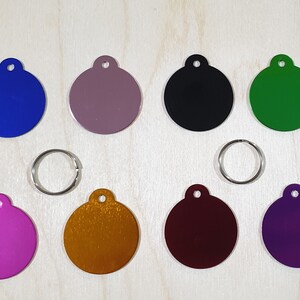 May include: Ten round metal tags in various colors, including blue, purple, green, black, gold, and red. The tags have a hole at the top for attaching to a key ring or other item.