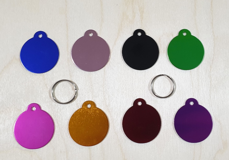 May include: Ten round metal tags in various colors, including blue, purple, green, black, gold, and red. The tags have a hole at the top for attaching to a key ring or other item.