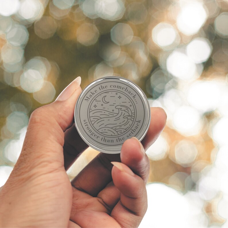 May include: A silver round token with the text "Make the comeback... stronger than the setback" and a graphic of a wave with a crescent moon and stars.