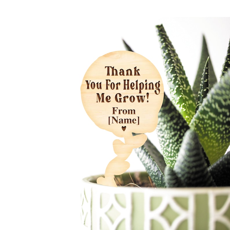 May include: Wooden plant stake with a speech bubble that says "Thank You For Helping Me Grow! From [Name]" with a small heart at the bottom. The stake is in a pot with a green succulent plant.
