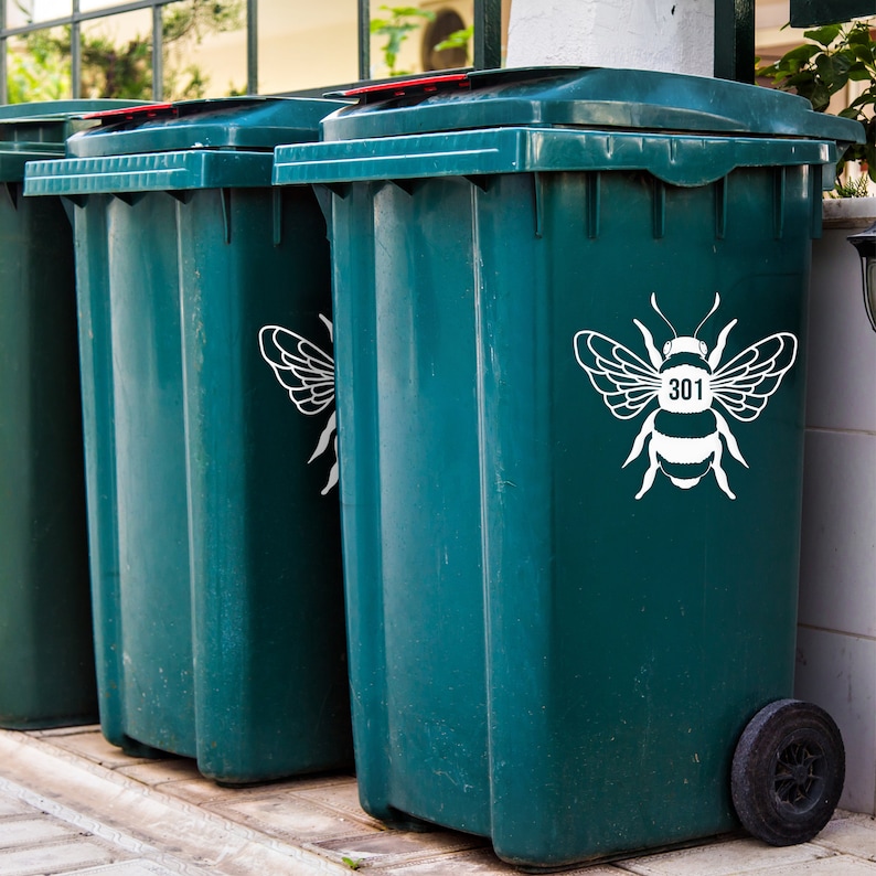 May include: Three green recycling bins with white bee decals. The bee on the rightmost bin has the number 301 on its body.