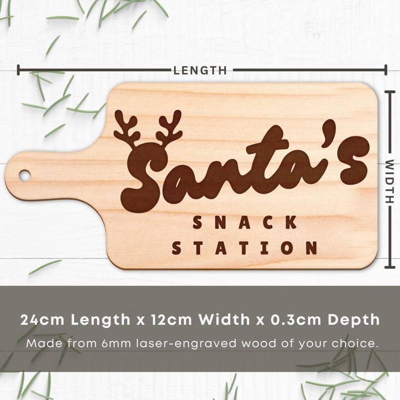 Op de afbeelding: Houten snijplank met handvat, lasergegraveerd met "Santa's SNACK STATION" in bruin. De plank is 24 cm lang, 12 cm breed en 0,3 cm diep. Voorzien van een rendiergeweihert ontwerp boven de tekst.