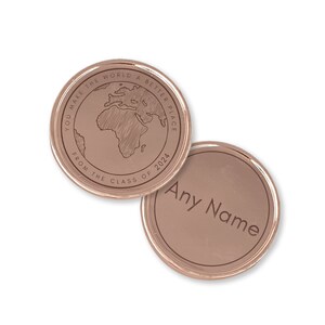 May include: Two rose gold colored metal coins. One coin features a world map with the text "You make the world a better place from the class of 2024". The other coin has the text "Any Name" in a circular design.