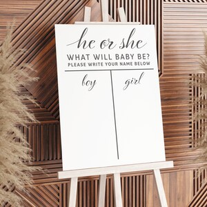 May include: A white sign on an easel with the text "he or she WHAT WILL BABY BE? PLEASE WRITE YOUR NAME BELOW" and two columns labeled "boy" and "girl".