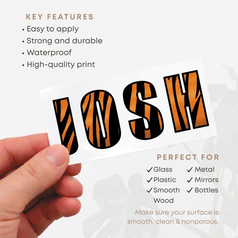 May include: A white sticker with the name "JOSH" in bold, black letters with orange tiger stripe fill. The sticker is held by a hand. The text on the sticker says it is easy to apply, strong, durable, waterproof, and has a high-quality print.