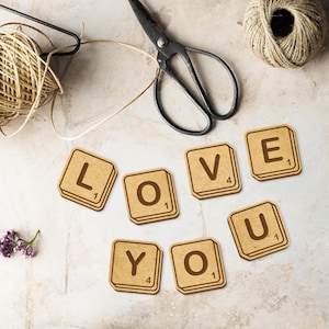 May include: A set of wooden Scrabble tiles spelling out the word "LOVE YOU". The tiles are arranged in a line on a light gray surface.