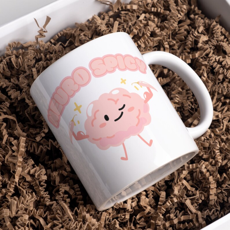 Puede incluir: Taza de cer&aacute;mica blanca con una ilustraci&oacute;n de cerebro rosa de dibujos animados y el texto "Neuro Spicy".