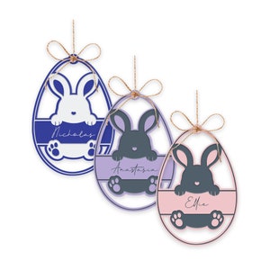 May include: Three Easter egg ornaments with bunny designs. Each egg is a different color: blue, purple, and pink. Each egg has a bunny cutout and a name: Nicholas, Anastasia, and Ellie. The ornaments are strung with twine.