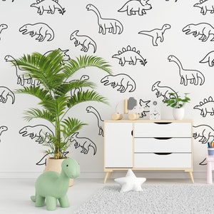 May include: A white wall with black dinosaur outlines, a green dinosaur toy, a potted palm tree, and a white dresser with three drawers.