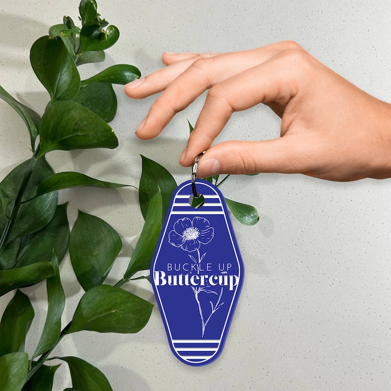 May include: Blue motel key tag with white stripes and a white outline of a flower with the text "Buckle Up Buttercup".