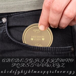 May include: A gold-colored decision coin with the words "Decision Coin" and "Julie" written on it. The coin is being held in a person's hand and is about to be placed in a pocket.