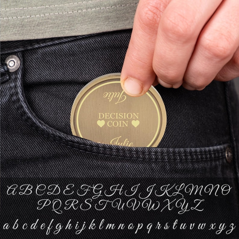 May include: A gold-colored decision coin with the words "Decision Coin" and "Julie" written on it. The coin is being held in a person's hand and is about to be placed in a pocket.